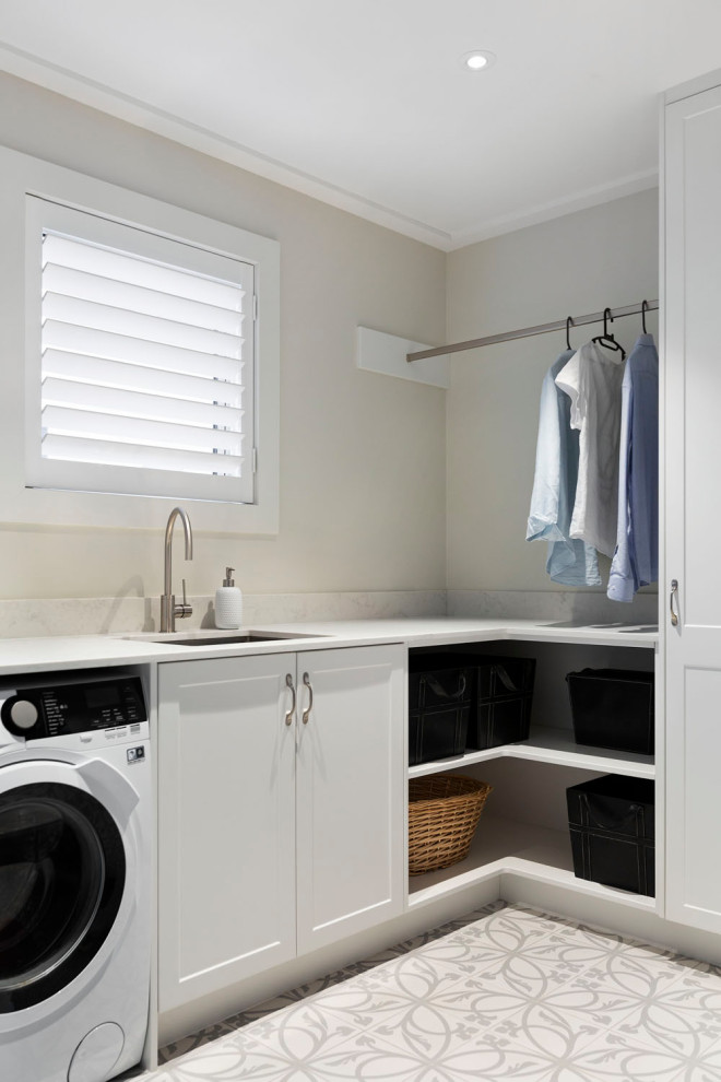 Mid-sized l-shaped dedicated laundry room in Auckland with a drop-in sink, open cabinets, white cabinets, quartz benchtops, white splashback, marble splashback, white walls, ceramic floors, a side-by-side washer and dryer, white floor and white benchtop.