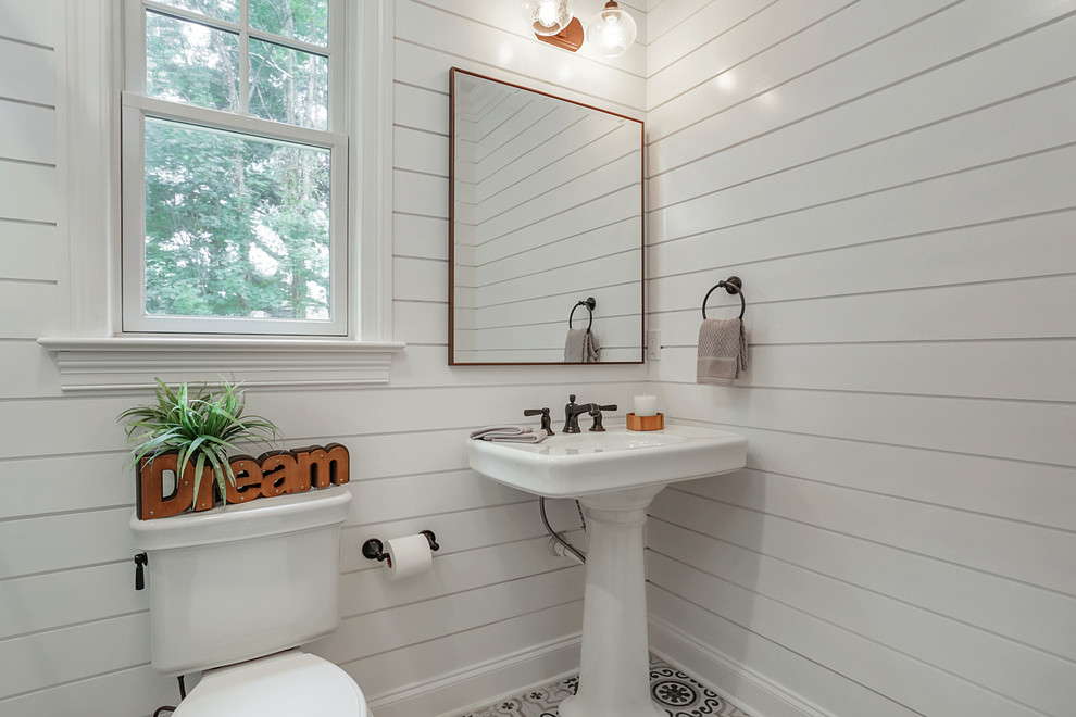 This is an example of a transitional powder room in New York with a two-piece toilet, white walls, cement tiles, a pedestal sink and multi-coloured floor.