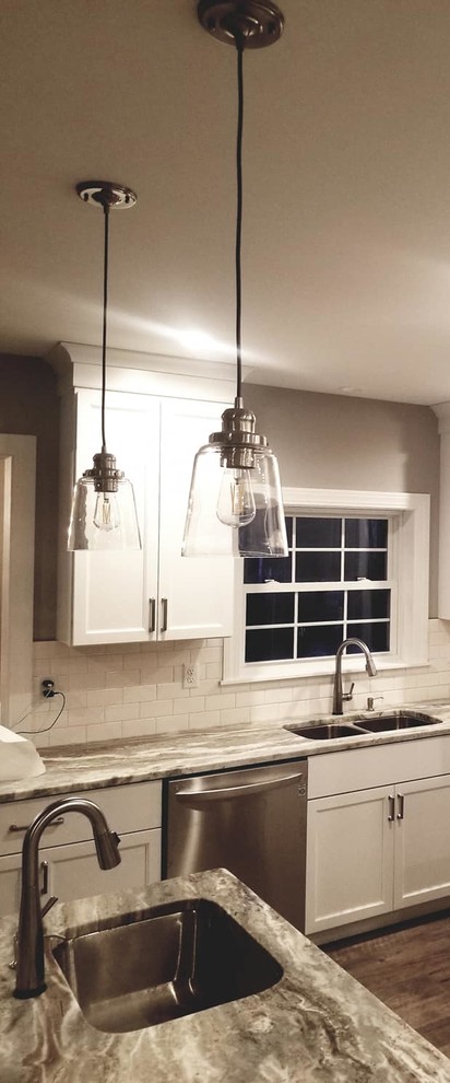 Transitional brown floor kitchen photo with an undermount sink, flat-panel cabinets, white cabinets, quartzite countertops, white backsplash, subway tile backsplash, stainless steel appliances and an island