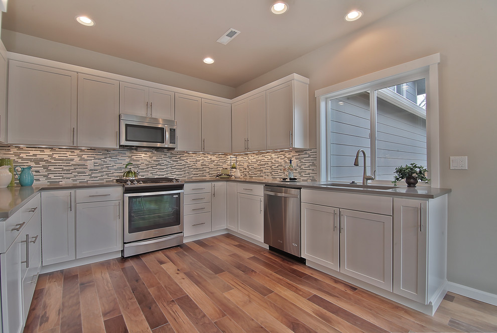 Photo of a mid-sized arts and crafts eat-in kitchen in Seattle with an undermount sink, shaker cabinets, white cabinets, quartz benchtops, glass tile splashback, stainless steel appliances, medium hardwood floors and no island.