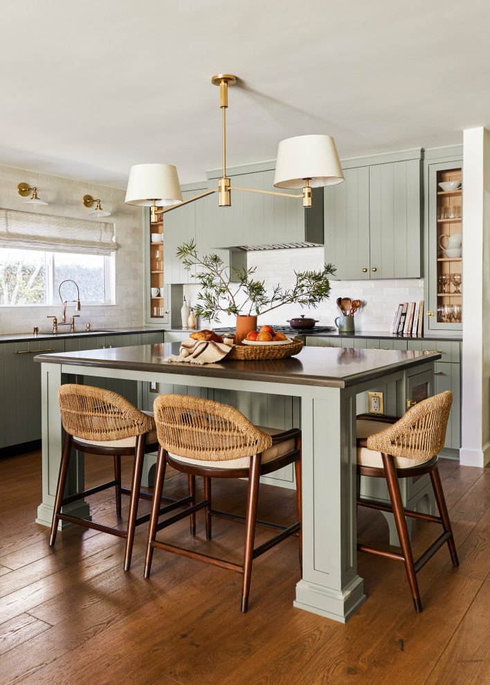 Inspiration for a transitional l-shaped kitchen in Los Angeles with an undermount sink, flat-panel cabinets, green cabinets, medium hardwood floors, with island, brown floor and black benchtop.