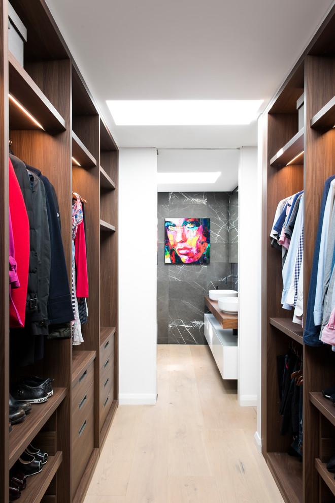 Mid-sized contemporary gender-neutral walk-in wardrobe in Sydney with open cabinets, dark wood cabinets, light hardwood floors and beige floor.