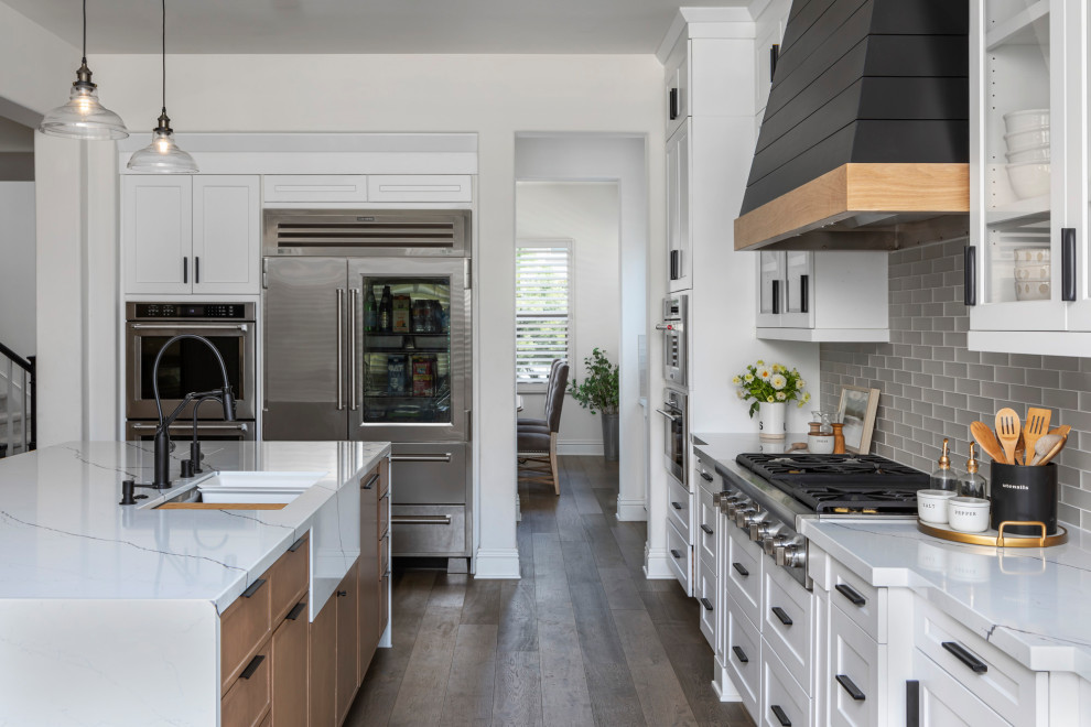 Inspiration for a small modern galley dark wood floor and brown floor open concept kitchen remodel in Orange County with a farmhouse sink, shaker cabinets, white cabinets, quartzite countertops, white backsplash, glass tile backsplash, stainless steel appliances, an island and white countertops