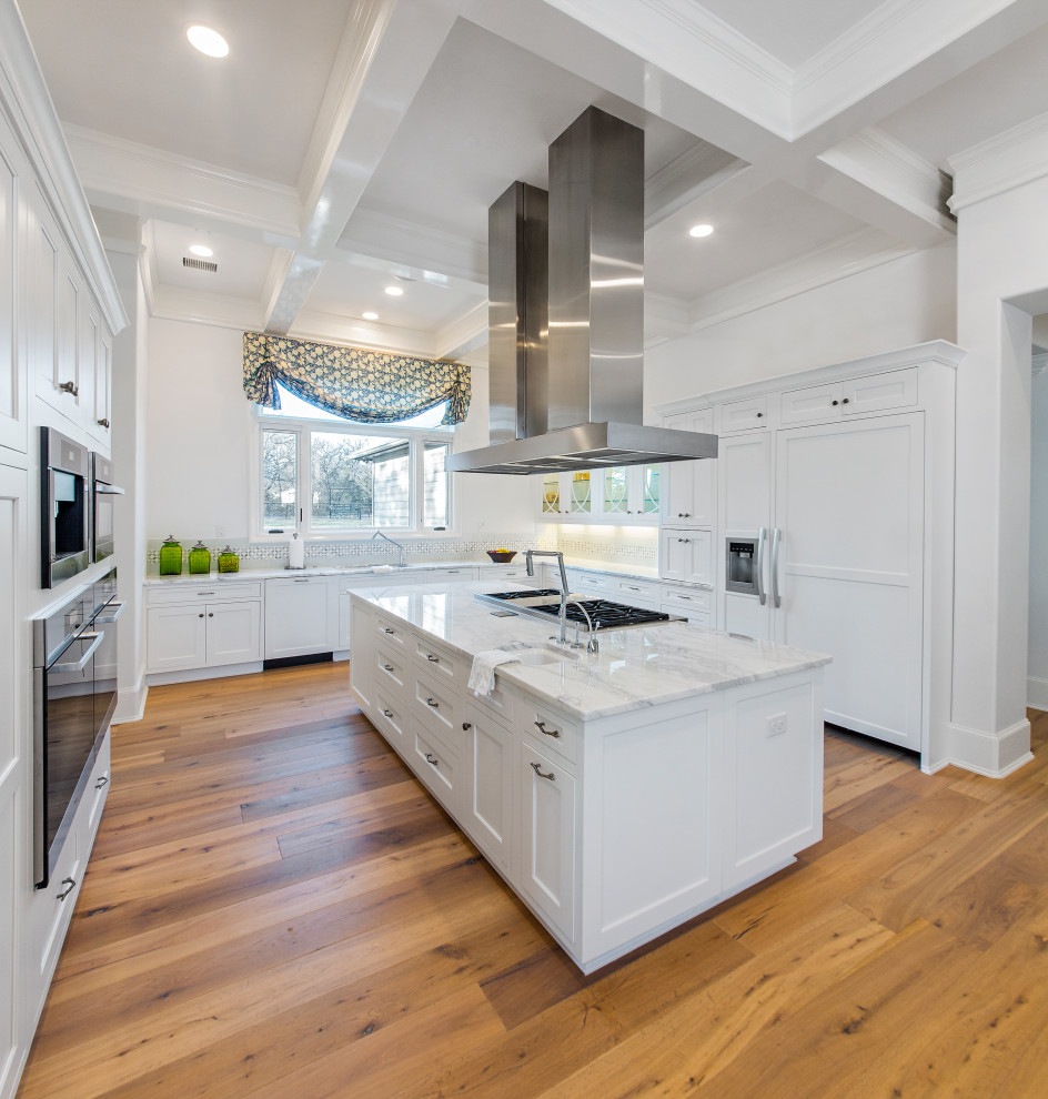 Photo of a large transitional l-shaped kitchen in Dallas with an undermount sink, shaker cabinets, white cabinets, marble benchtops, white splashback, subway tile splashback, stainless steel appliances, medium hardwood floors, with island, brown floor, white benchtop and coffered.