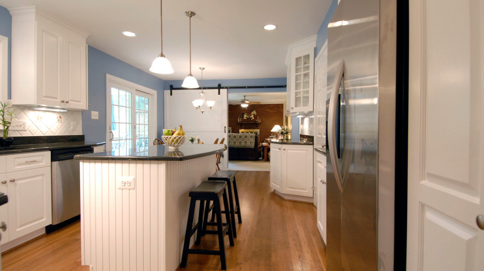 ボストンにある中くらいなカントリー風のおしゃれなキッチン (ドロップインシンク、レイズドパネル扉のキャビネット、白いキャビネット、オニキスカウンター、白いキッチンパネル、セラミックタイルのキッチンパネル、シルバーの調理設備、淡色無垢フローリング、茶色い床、黒いキッチンカウンター) の写真
