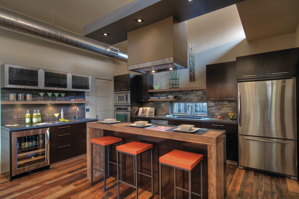 Example of a small transitional galley medium tone wood floor and brown floor open concept kitchen design with an undermount sink, flat-panel cabinets, dark wood cabinets, concrete countertops, gray backsplash, ceramic backsplash, stainless steel appliances, an island and gray countertops