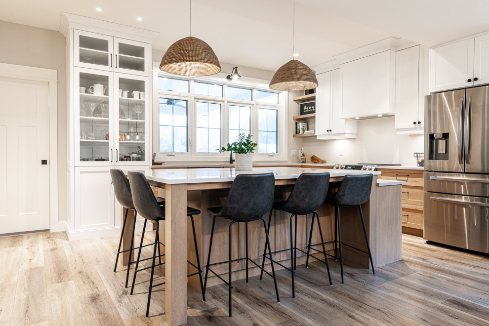 Example of a mid-sized transitional l-shaped laminate floor and brown floor eat-in kitchen design in Toronto with an undermount sink, recessed-panel cabinets, white cabinets, quartz countertops, stainless steel appliances, an island and white countertops