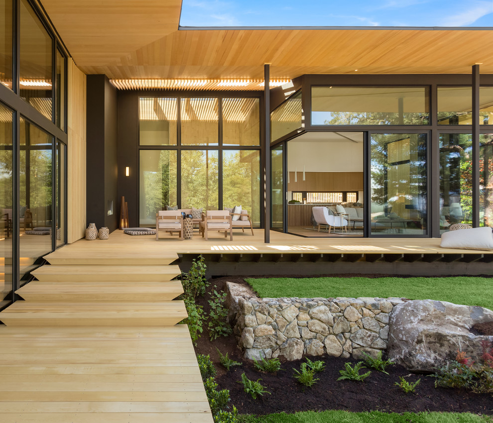 This is an example of an expansive contemporary backyard deck in Portland with a fire feature and a roof extension.