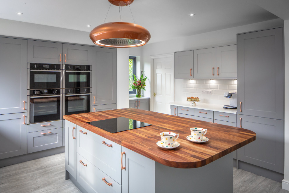 Photo of a large classic u-shaped kitchen/diner in Other with a submerged sink, shaker cabinets, grey cabinets, wood worktops, white splashback, ceramic splashback, black appliances, vinyl flooring, an island, grey floors and white worktops.