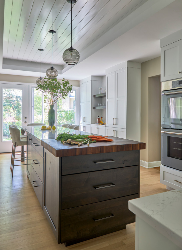 Inspiration for a large transitional u-shaped light wood floor, brown floor and coffered ceiling eat-in kitchen remodel in Chicago with a farmhouse sink, shaker cabinets, white cabinets, quartz countertops, white backsplash, subway tile backsplash, stainless steel appliances, an island and multicolored countertops