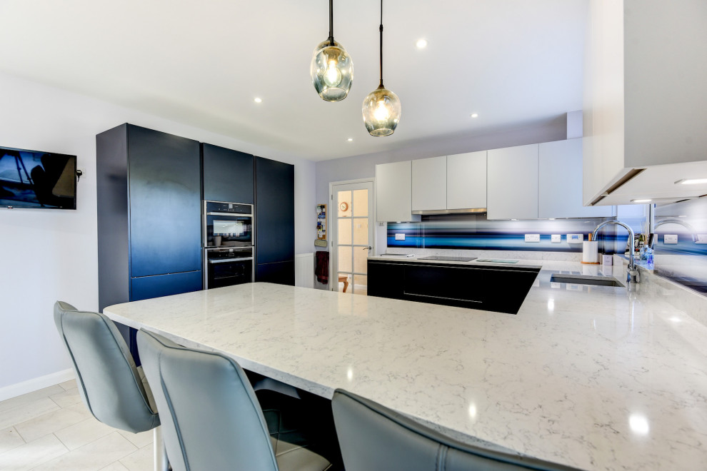 Large modern u-shaped eat-in kitchen in Sussex with an undermount sink, flat-panel cabinets, blue cabinets, quartzite benchtops, blue splashback, glass sheet splashback, black appliances, vinyl floors, a peninsula, white floor and white benchtop.
