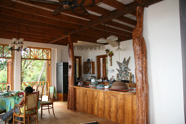 Photo of a large tropical galley open plan kitchen in Other with a double-bowl sink, flat-panel cabinets, light wood cabinets, wood benchtops, black appliances and a peninsula.