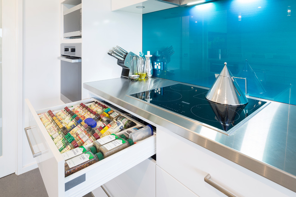 Inspiration for a mid-sized modern galley kitchen pantry in Canberra - Queanbeyan with flat-panel cabinets, white cabinets, stainless steel benchtops, blue splashback, glass sheet splashback, ceramic floors, with island, grey floor and multi-coloured benchtop.