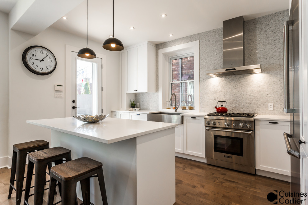 Eat-in kitchen - mid-sized transitional l-shaped medium tone wood floor eat-in kitchen idea in Montreal with a farmhouse sink, shaker cabinets, white cabinets, quartzite countertops, white backsplash, mosaic tile backsplash, stainless steel appliances and an island
