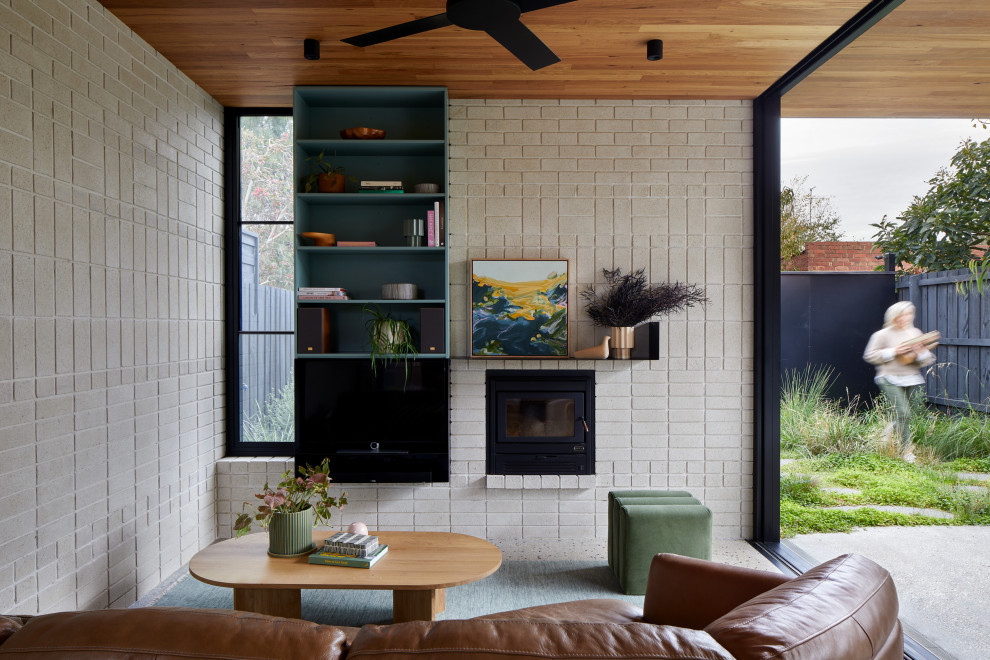 Immagine di un piccolo soggiorno minimalista aperto con pareti grigie, pavimento in cemento, stufa a legna, cornice del camino in metallo, TV nascosta, pavimento grigio, soffitto in legno e pareti in mattoni
