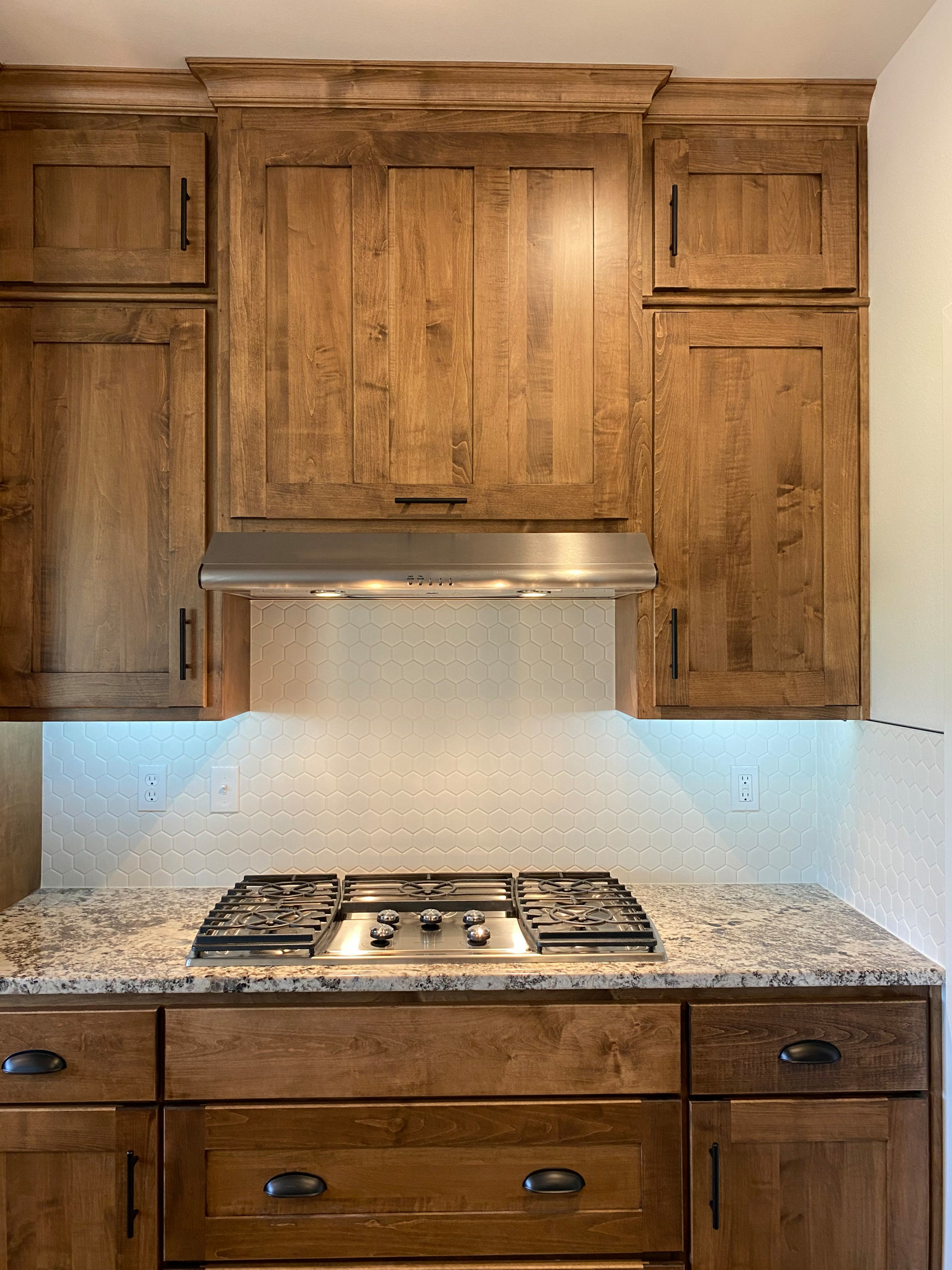 Custom kitchen cabinetry with gas stove top and brushed nickel exhaust vent