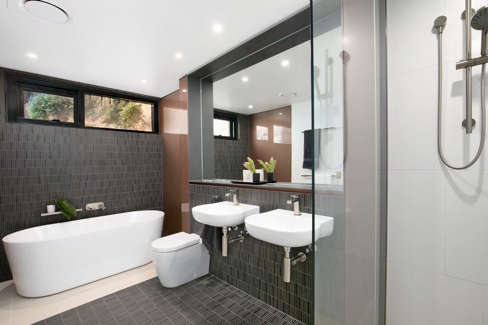 Design ideas for a contemporary master bathroom in Sydney with a one-piece toilet, gray tile, brown walls, a freestanding tub, an open shower, matchstick tile, a wall-mount sink, multi-coloured floor, an open shower, wood benchtops and brown benchtops.