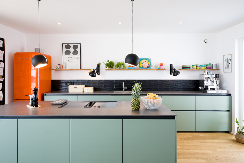 Design ideas for a mid-sized contemporary galley open plan kitchen in Stuttgart with flat-panel cabinets, with island, an undermount sink, green cabinets, black splashback, subway tile splashback, coloured appliances, light hardwood floors, beige floor and grey benchtop.