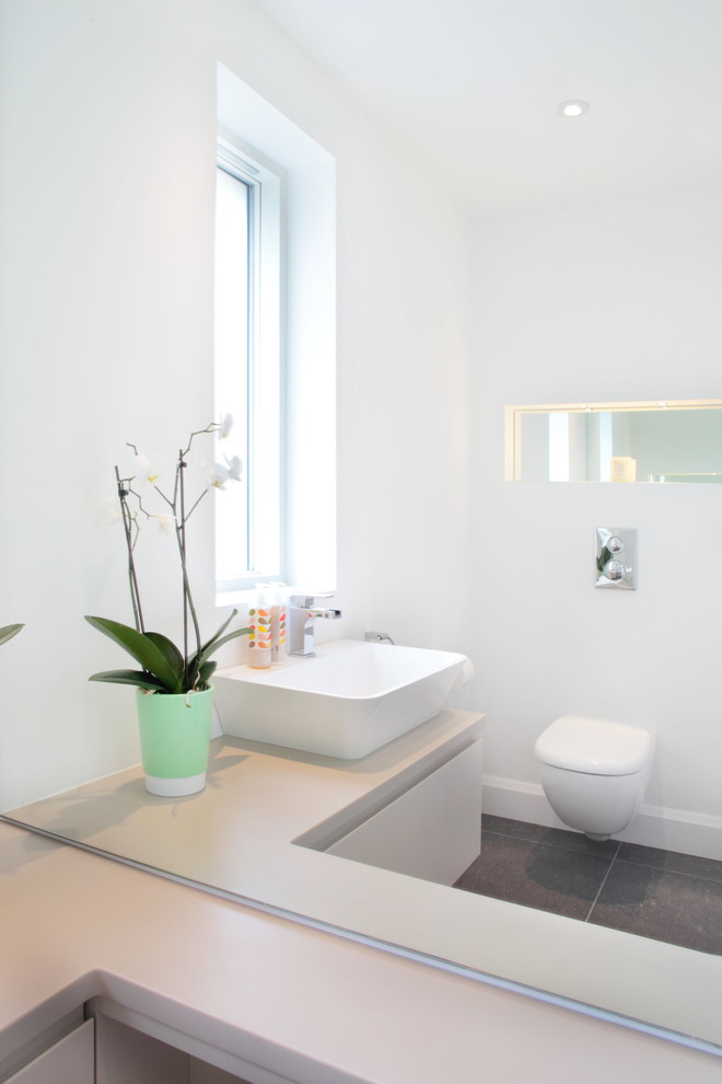 This is an example of a contemporary bathroom in Buckinghamshire with flat-panel cabinets, beige cabinets, a wall-mount toilet, white walls, slate floors and a vessel sink.