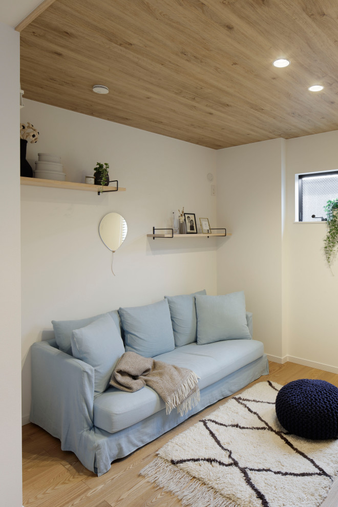 На фото: открытая гостиная комната среднего размера в скандинавском стиле с белыми стенами, светлым паркетным полом, отдельно стоящим телевизором, бежевым полом, потолком с обоями, обоями на стенах и синим диваном без камина