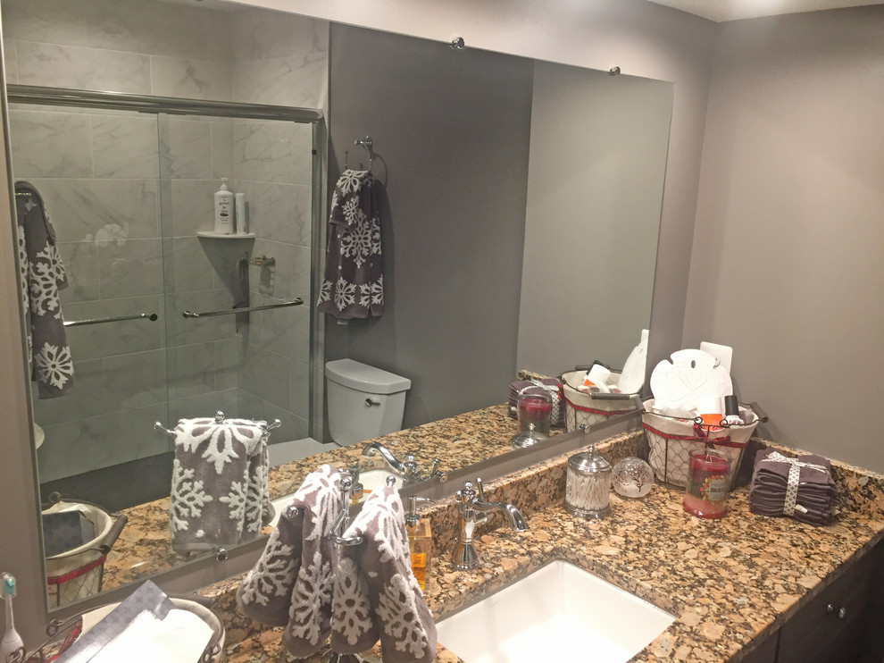 Inspiration for a mid-sized transitional master bathroom in DC Metro with recessed-panel cabinets, brown cabinets, an alcove shower, a two-piece toilet, gray tile, porcelain tile, grey walls, porcelain floors, an undermount sink, granite benchtops, grey floor, a sliding shower screen and brown benchtops.