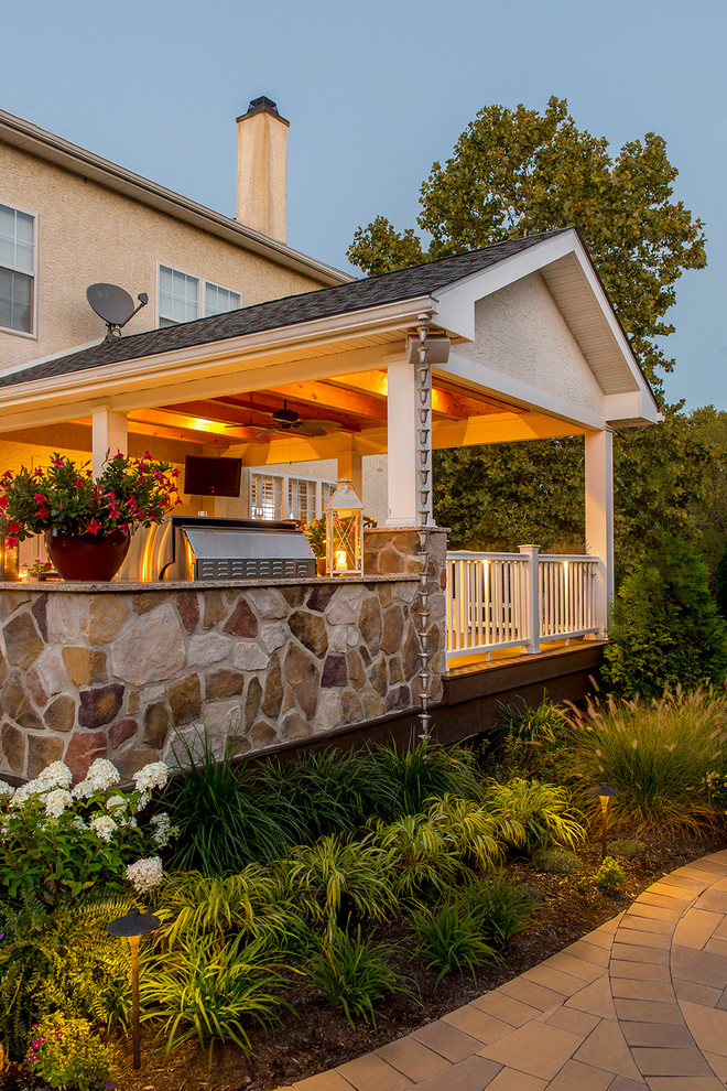 This is an example of a mid-sized traditional backyard deck in Philadelphia with an outdoor kitchen and a roof extension.