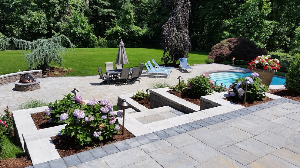 Large traditional backyard custom-shaped lap pool in New York with natural stone pavers.