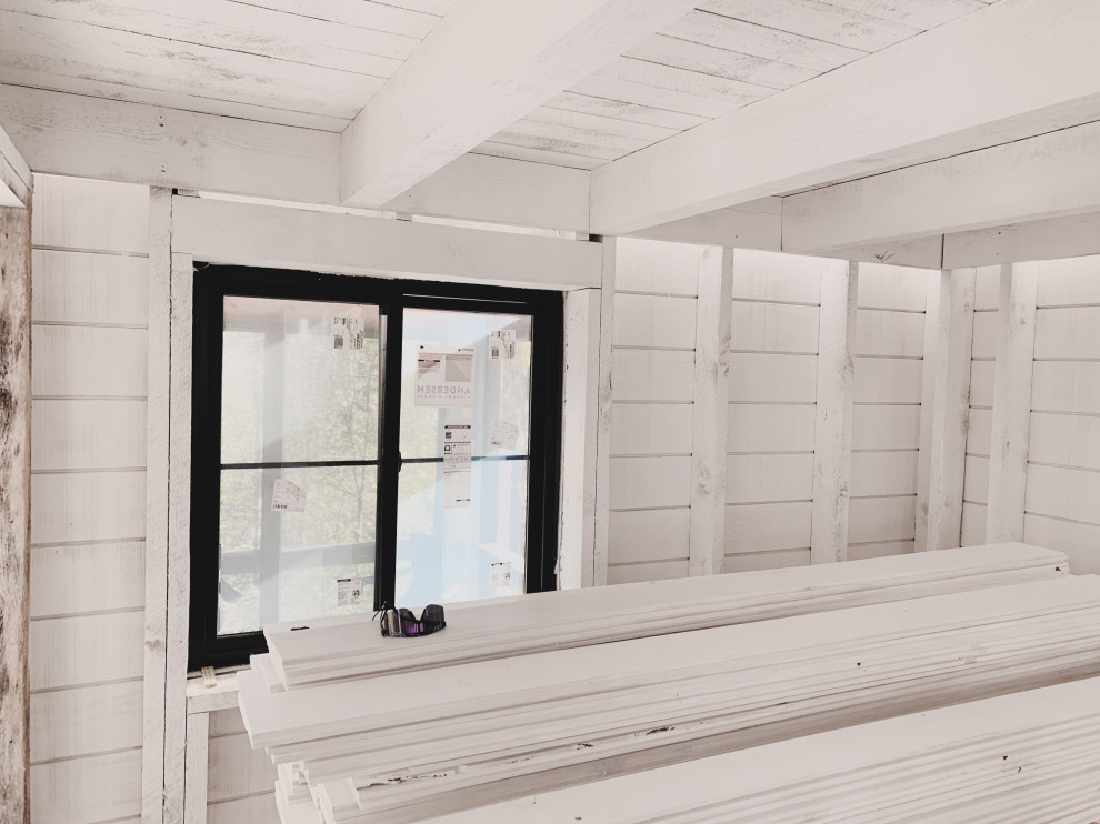 Kleines Rustikales Gästezimmer mit weißer Wandfarbe, hellem Holzboden, Kaminofen, Kaminumrandung aus Holzdielen, beigem Boden, freigelegten Dachbalken und Holzdielenwänden in Minneapolis