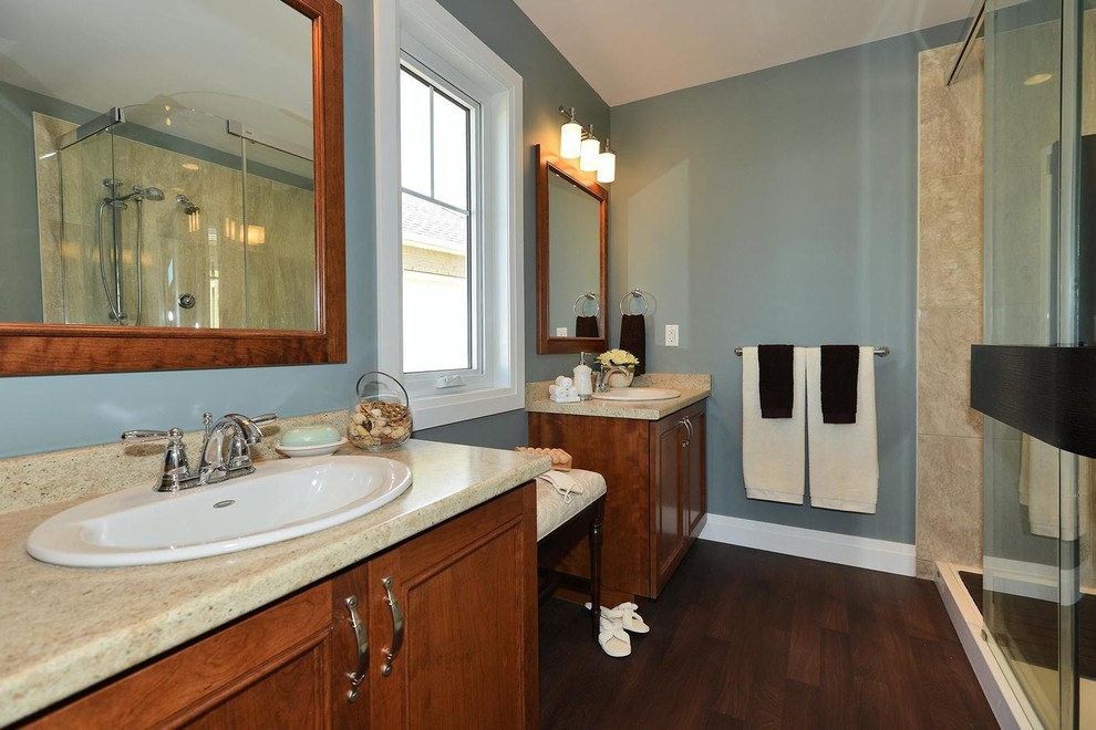 Large transitional master bathroom in Toronto with beaded inset cabinets, medium wood cabinets, a corner shower, a two-piece toilet, blue walls, dark hardwood floors, a drop-in sink, limestone benchtops, brown floor, a sliding shower screen and multi-coloured benchtops.