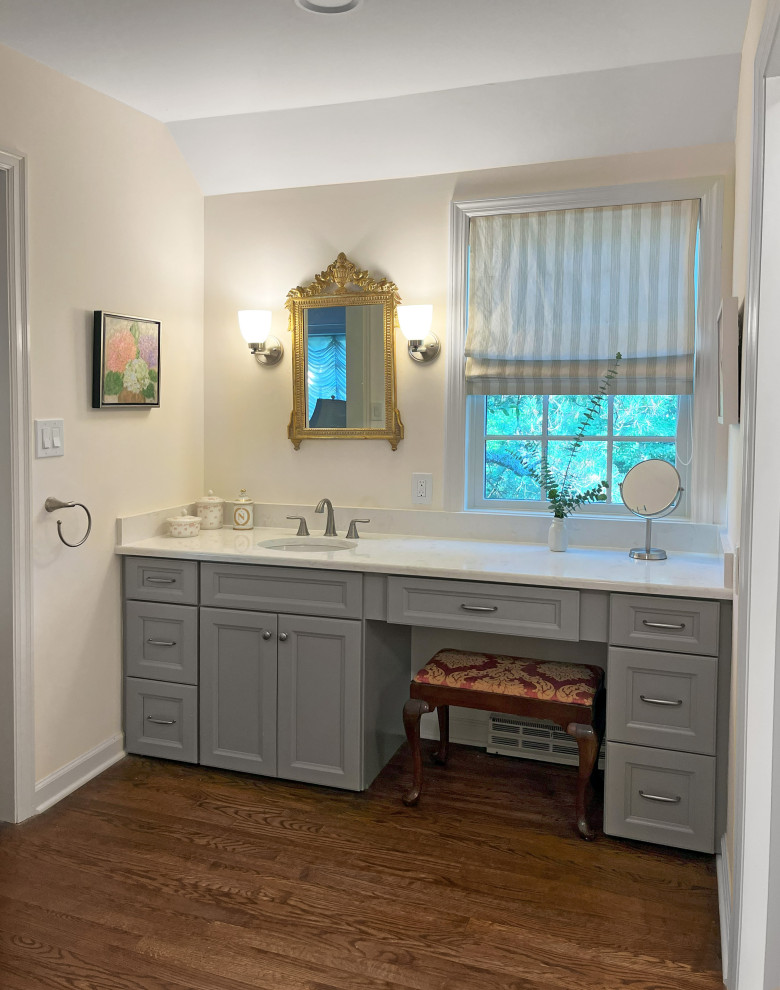 Design ideas for a large transitional master bathroom in Philadelphia with recessed-panel cabinets, grey cabinets, a corner shower, a one-piece toilet, beige tile, porcelain tile, beige walls, porcelain floors, an undermount sink, quartzite benchtops, grey floor, a hinged shower door, white benchtops, a shower seat and a double vanity.