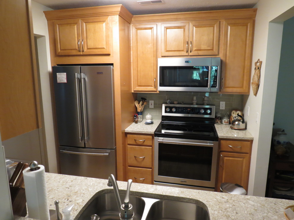 Small transitional galley vinyl floor and brown floor enclosed kitchen photo with an undermount sink, raised-panel cabinets, light wood cabinets, quartz countertops, beige backsplash, glass tile backsplash, stainless steel appliances, no island and beige countertops