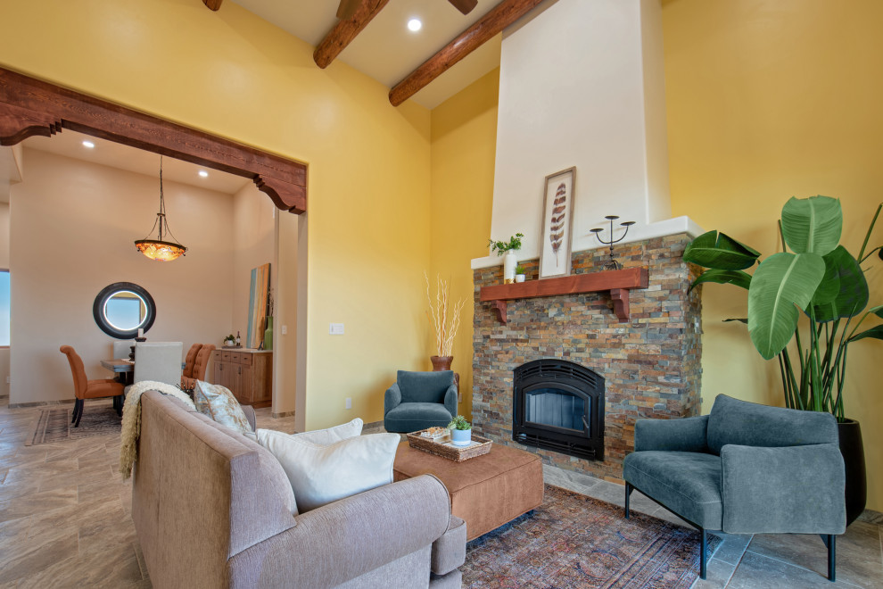 Idée de décoration pour un salon sud-ouest américain de taille moyenne avec un mur multicolore, un sol en travertin, une cheminée standard, un manteau de cheminée en pierre de parement, un sol beige et poutres apparentes.