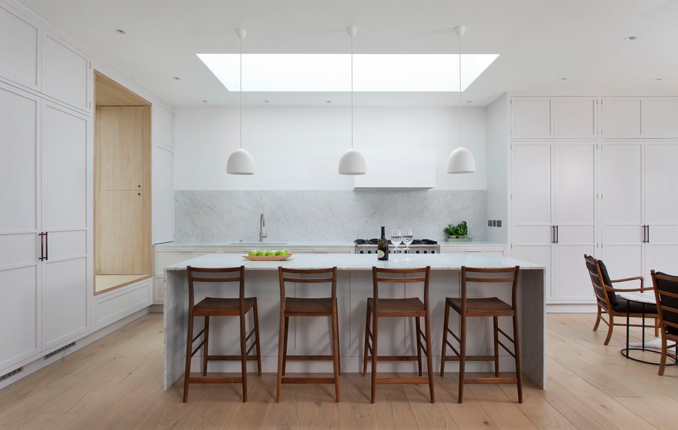 Photo of a mid-sized contemporary open plan kitchen in Dublin with recessed-panel cabinets, white cabinets, marble benchtops, grey splashback, marble splashback, with island, beige floor, grey benchtop, stainless steel appliances and light hardwood floors.