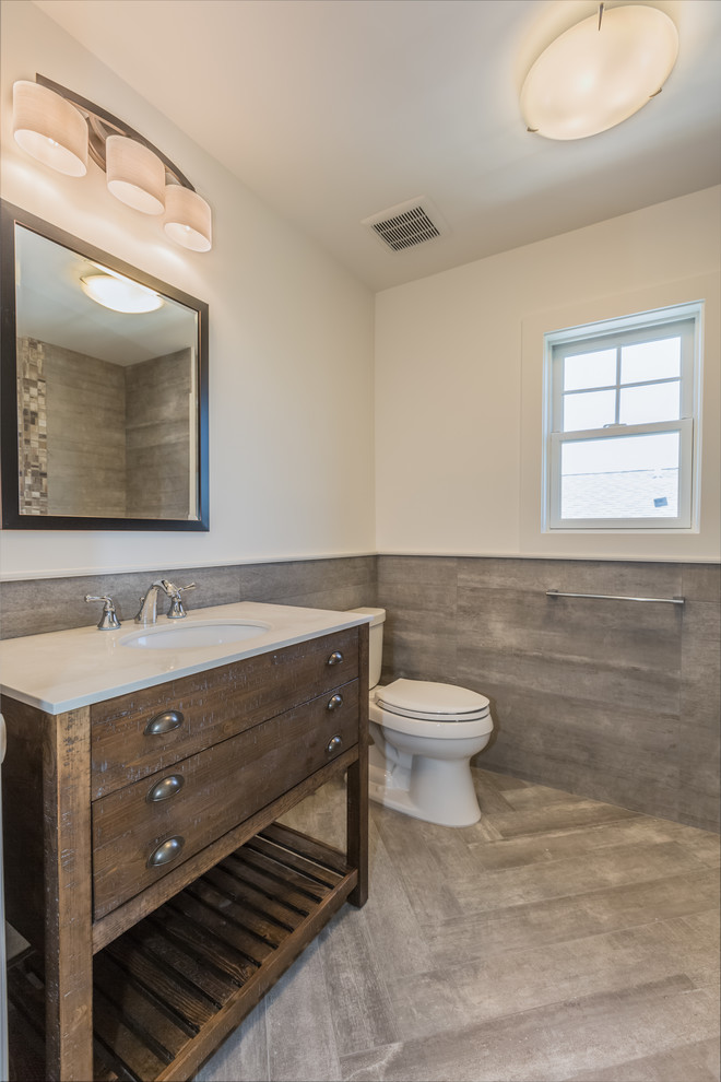 This is an example of a mid-sized contemporary 3/4 bathroom in New York with furniture-like cabinets, medium wood cabinets, an alcove tub, a shower/bathtub combo, a two-piece toilet, gray tile, porcelain tile, multi-coloured walls, porcelain floors, an integrated sink, grey floor, a shower curtain and beige benchtops.