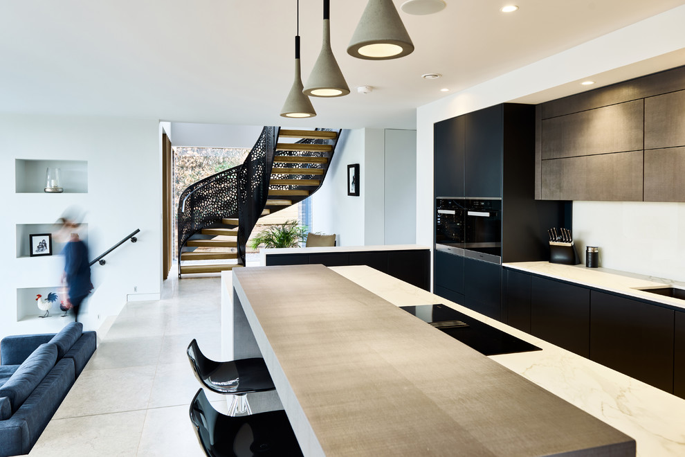 Photo of a contemporary open plan kitchen in Devon with an undermount sink, flat-panel cabinets, black cabinets, white splashback, black appliances, with island, grey floor and white benchtop.