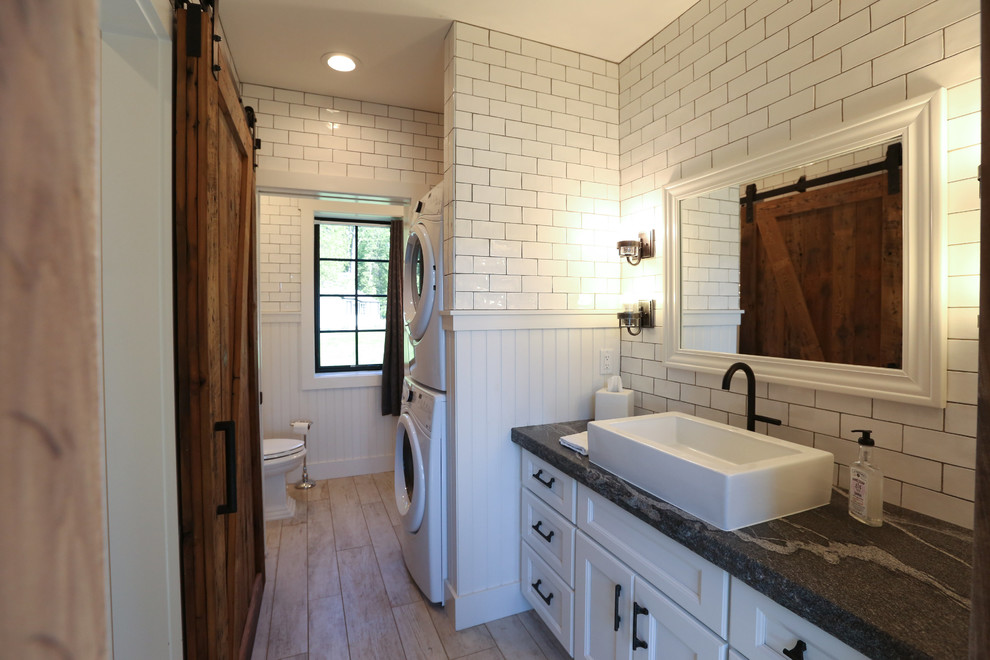 This is an example of a mid-sized transitional master bathroom in Other with recessed-panel cabinets, white cabinets, an open shower, a two-piece toilet, white tile, subway tile, white walls, light hardwood floors, a vessel sink and soapstone benchtops.