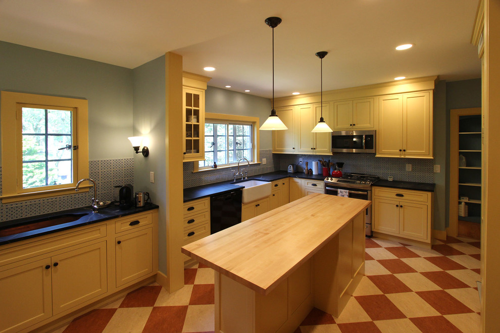 Photo of a mid-sized traditional l-shaped kitchen in Other with a farmhouse sink, flat-panel cabinets, yellow cabinets, soapstone benchtops, blue splashback, ceramic splashback, linoleum floors and with island.