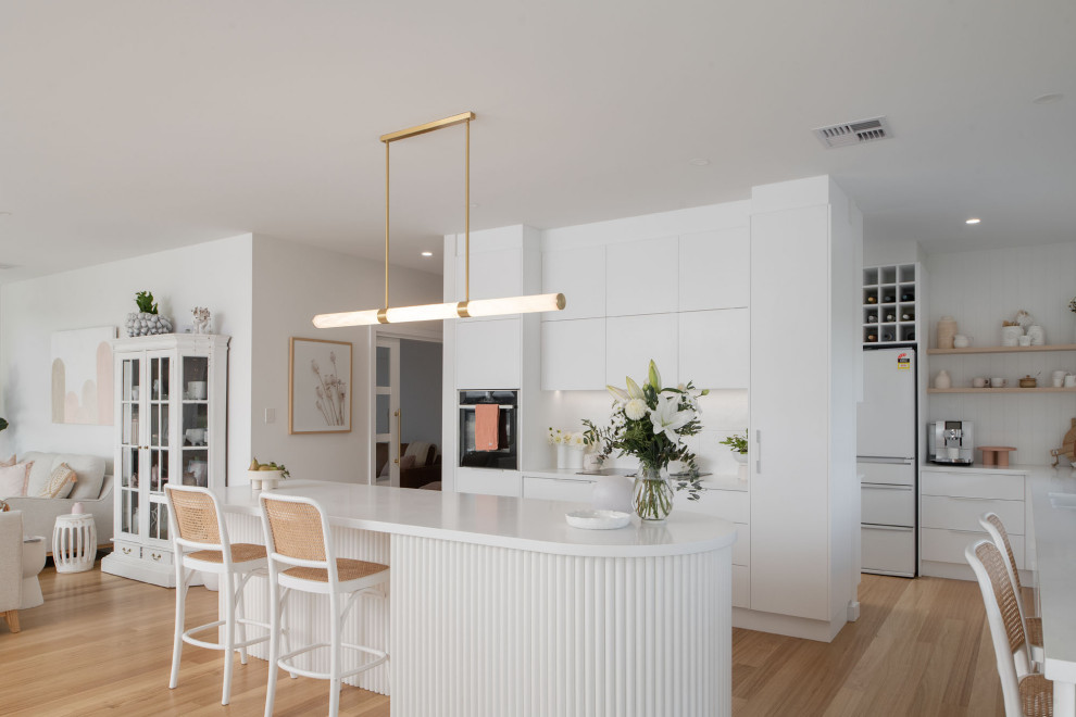 Photo of a beach style u-shaped kitchen in Hobart with flat-panel cabinets, white cabinets, black appliances, light hardwood floors, with island, beige floor and white benchtop.