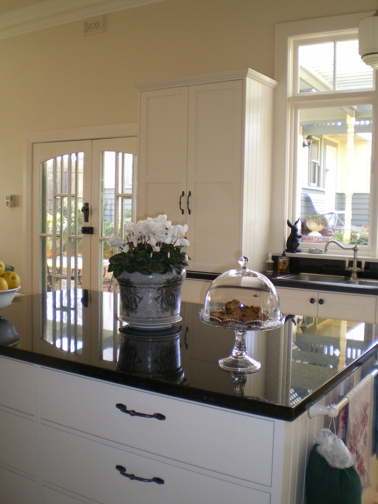 Photo of a mediterranean l-shaped eat-in kitchen in Geelong with a double-bowl sink, shaker cabinets, white cabinets, granite benchtops, black splashback, glass sheet splashback, coloured appliances, light hardwood floors and with island.