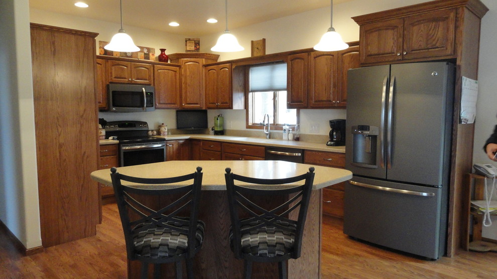 Inspiration for a mid-sized u-shaped medium tone wood floor open concept kitchen remodel with an undermount sink, raised-panel cabinets, medium tone wood cabinets, solid surface countertops, stainless steel appliances, beige walls and an island