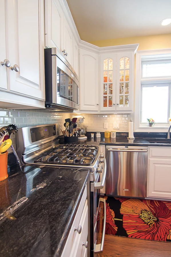 Eat-in kitchen - large transitional u-shaped medium tone wood floor and brown floor eat-in kitchen idea with an undermount sink, raised-panel cabinets, white cabinets, quartzite countertops, white backsplash, glass tile backsplash, stainless steel appliances, an island and black countertops