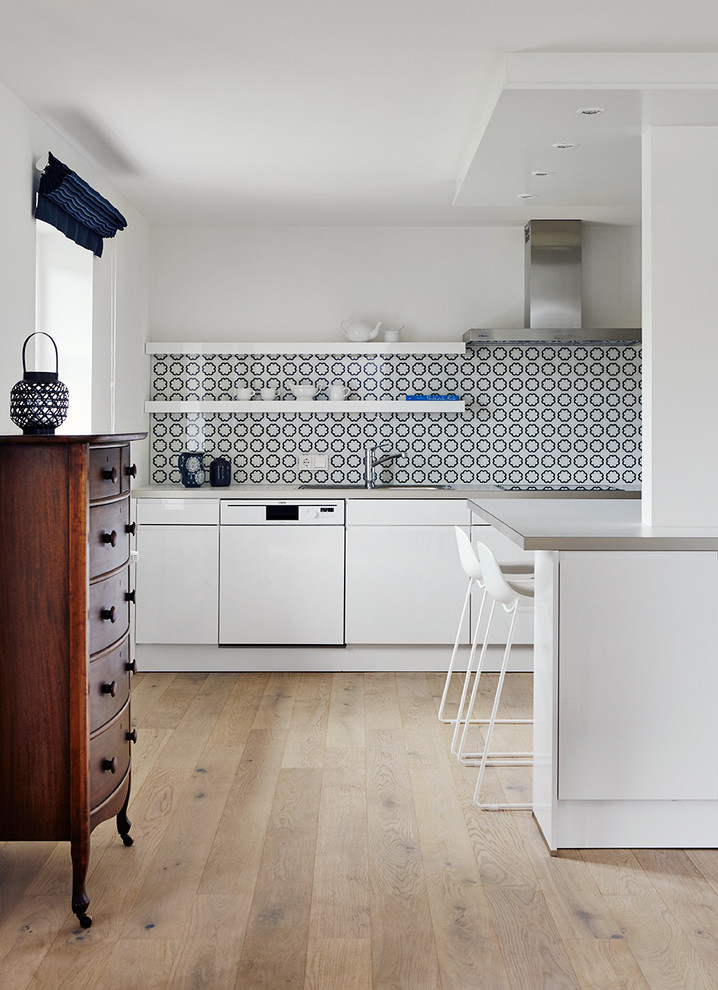 This is an example of a mid-sized eclectic open plan kitchen in Other with a drop-in sink, flat-panel cabinets, white cabinets, blue splashback, porcelain splashback, light hardwood floors, stainless steel appliances, stainless steel benchtops and no island.
