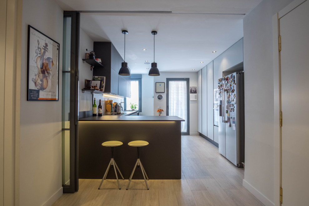 This is an example of a mid-sized contemporary l-shaped open plan kitchen in Madrid with an undermount sink, recessed-panel cabinets, quartz benchtops, brown splashback, timber splashback, stainless steel appliances, ceramic floors, a peninsula, beige floor and black benchtop.