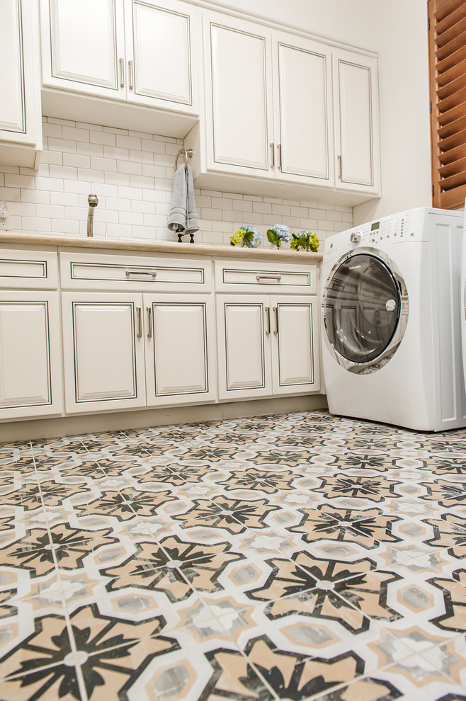 Inspiration for a large transitional l-shaped laundry room in Phoenix with an undermount sink, raised-panel cabinets, white cabinets, solid surface benchtops, white walls, terra-cotta floors and a side-by-side washer and dryer.