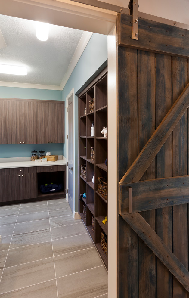 Photo of a large transitional l-shaped utility room in Tampa with a farmhouse sink, flat-panel cabinets, dark wood cabinets, solid surface benchtops, blue walls, ceramic floors, a side-by-side washer and dryer, multi-coloured floor and white benchtop.