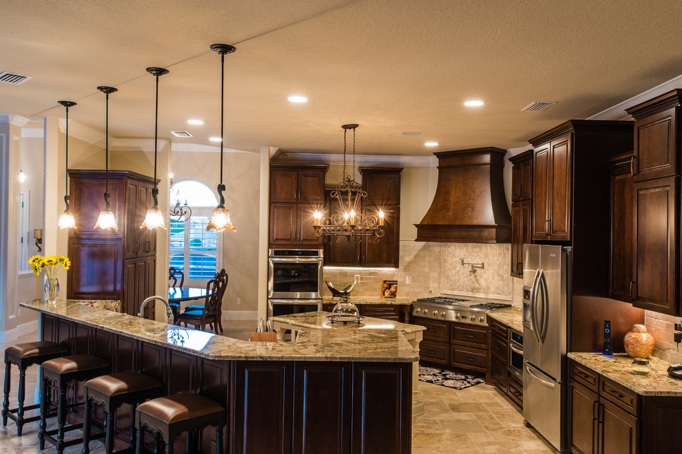 Large transitional l-shaped travertine floor and beige floor enclosed kitchen photo in Orlando with an undermount sink, raised-panel cabinets, dark wood cabinets, granite countertops, beige backsplash, mosaic tile backsplash, stainless steel appliances and an island