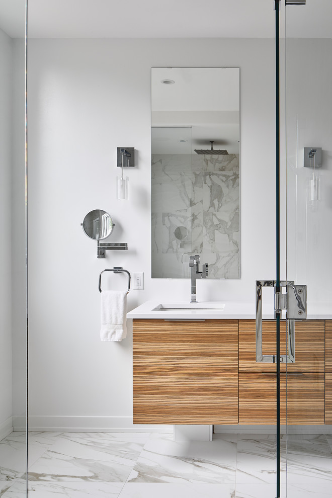 This is an example of a mid-sized modern master bathroom in Ottawa with flat-panel cabinets, light wood cabinets, a freestanding tub, a corner shower, a one-piece toilet, gray tile, ceramic tile, white walls, porcelain floors, an undermount sink, engineered quartz benchtops, white floor, a hinged shower door and white benchtops.