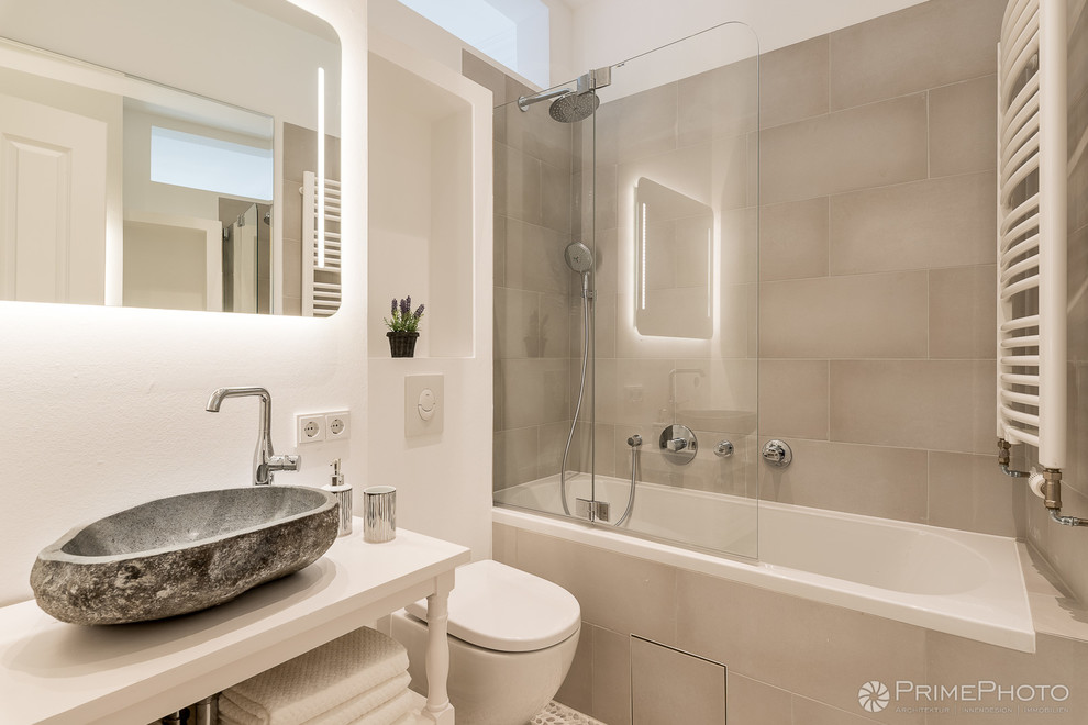 Design ideas for a small tropical bathroom in Berlin with open cabinets, a drop-in tub, a shower/bathtub combo, a two-piece toilet, beige tile, ceramic tile, white walls, pebble tile floors, a vessel sink, granite benchtops, beige floor and a hinged shower door.