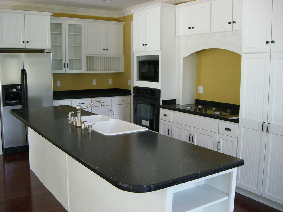 Photo of a mid-sized galley eat-in kitchen in Other with a double-bowl sink, white cabinets, solid surface benchtops, stainless steel appliances, dark hardwood floors, with island and recessed-panel cabinets.