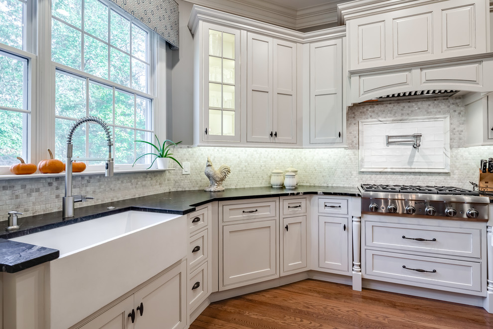 This is an example of a large transitional u-shaped eat-in kitchen in Philadelphia with a farmhouse sink, recessed-panel cabinets, white cabinets, soapstone benchtops, grey splashback, mosaic tile splashback, stainless steel appliances, dark hardwood floors, with island, brown floor and black benchtop.